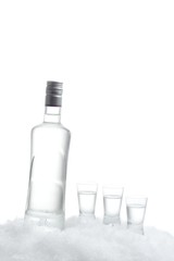 Bottle of vodka with glasses standing on ice on white background