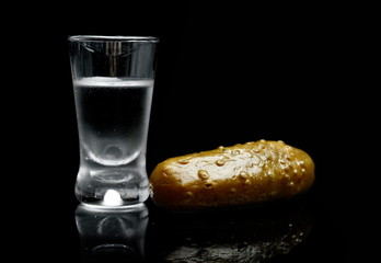 Glass of vodka with pickled cucumber isolated on black