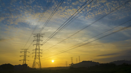 Silhouetted electricity transmition pylons against sunrise.