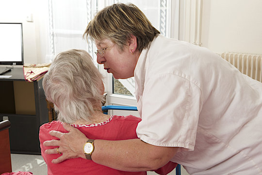 Cheerful care giver helping elderly woman at home, embracing her