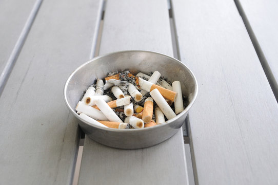 Many used cigarettes in aluminium ashtray on wooden table
