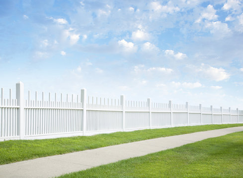 White Fence, Grass, Sidewalk, Blue Sky And Clouds