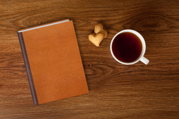 woman with cup of tea, cookies and book on wood