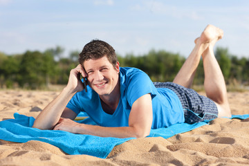 Fototapeta premium Junger Mann mit Smart Phone am Strand