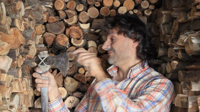 woodcutter sharpening an axe , huge firewood pile
