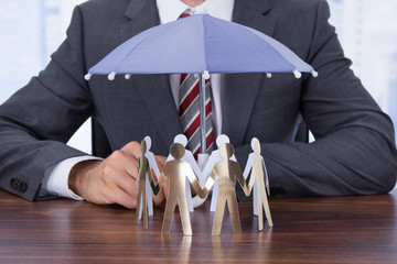 Businessman Sheltering Paper People With Umbrella