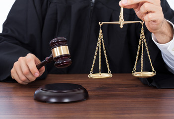 Judge Holding Weight Scale While Striking Gavel At Desk