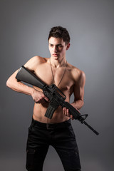Fototapeta premium Handsome bare-chested soldier is holding a rifle