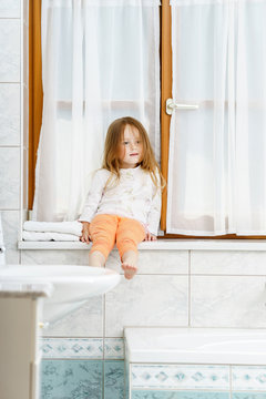 Cute little girl sitting on a bathroom window