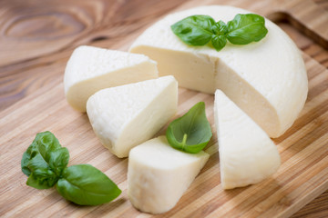 Wooden cutting board with sliced round cheese and green basil