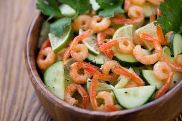 Salad with roasted shrimps, cucumbers and lime in a wooden bowl