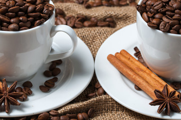 Two white coffee cups with coffee beans, cinnamon and aniseed.