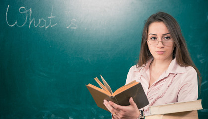 young female teacher at blackboard with open book