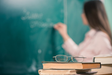 Fototapeta glasses and books with teacher writing at blackboard obraz