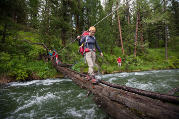 Backpackers are crossing mountain river by wooden log in Altai m