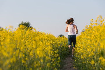 Fototapeta premium Young woman is jogging in yellow rapeseed field at sunset