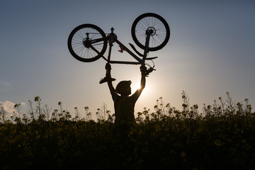 Mtb biker is holding bicycle above his head in yellow rapeseed f