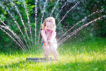 Happy girl playing with garden sprinkler