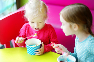 Two cute little sisters eating ice cream together