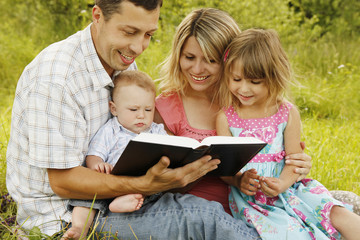 young family reading the Bible in nature