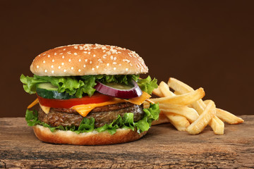Tasty hamburger and french frites on wood background.