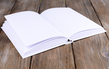 Open white book on wooden table, close-up