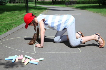 Cute girl drawing with chalk on asphalt