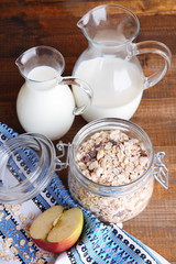 Homemade granola in glass jar, jugs with milk and fresh apple,