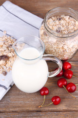 Homemade granola in glass jar, fresh cherries and jug with milk