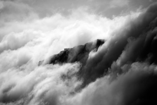 Fototapeta Black and white cliff appearing through clouds