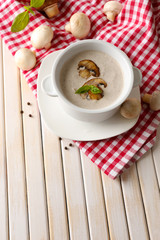 Mushroom soup in white pot, on napkin, on wooden background