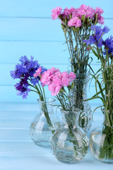 Beautiful summer flowers in vases on blue wooden background