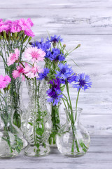 Beautiful summer flowers in vases on grey wooden background