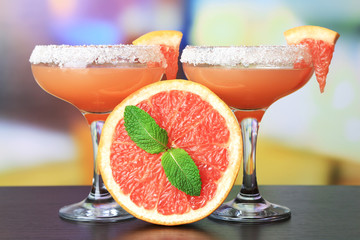 Grapefruit cocktail in glasses on bright background