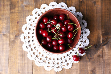 Cherries in color bowl on wooden background