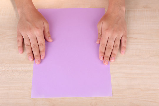 Woman hands and color paper for origami on wooden table