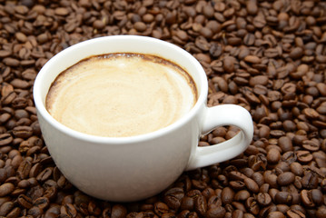 cup of coffee with cream on a coffee beans background