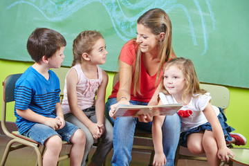 Child care worker and children reading book in kindergarten