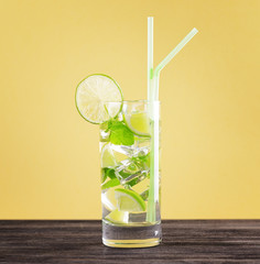 Glass of mojito cocktail on pastel yellow background