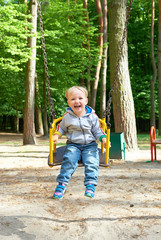Happy little blond boy having fun on a swing.
