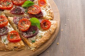 delicious pizza with salami and tomatoes on a wooden background
