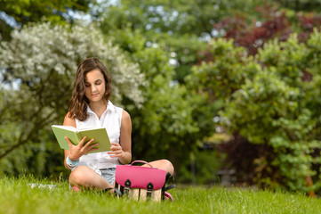 Naklejka na ściany i meble Teenage girl reading book sitting in park