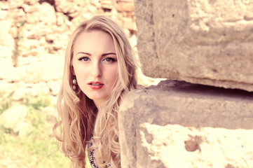 Beautiful blond woman leaning against ancient stone wall