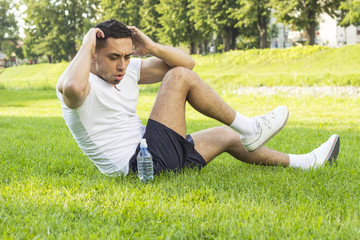 Fitness man exercising sit up outside in grass in summer
