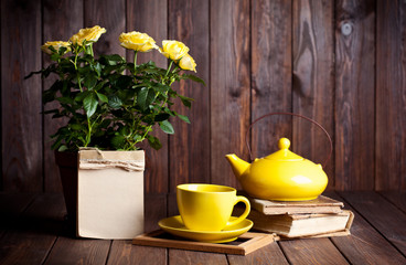 yellow roses in pot, tеapot, tea cup and old books on wooden ta