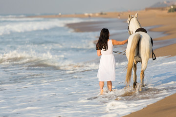 rear view of young woman walking a horse on beach