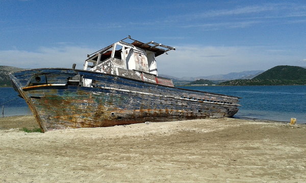 shipwrecked boat beached on sand with sea and mountains