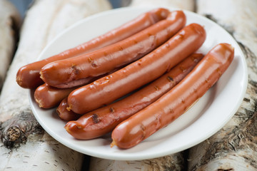 Glass plate with grilled sausages on firewood, studio shot
