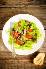 green salad with tomatoes and roast beef in a white dish