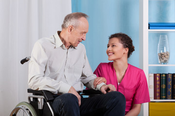 Obraz premium Nurse smiles to sitting in a wheelchair patient